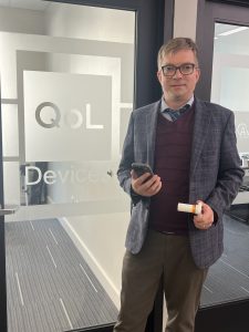 Richard Hinds standing in front of his door in Rochester MN - the QoL Devices Logo is etched on the door