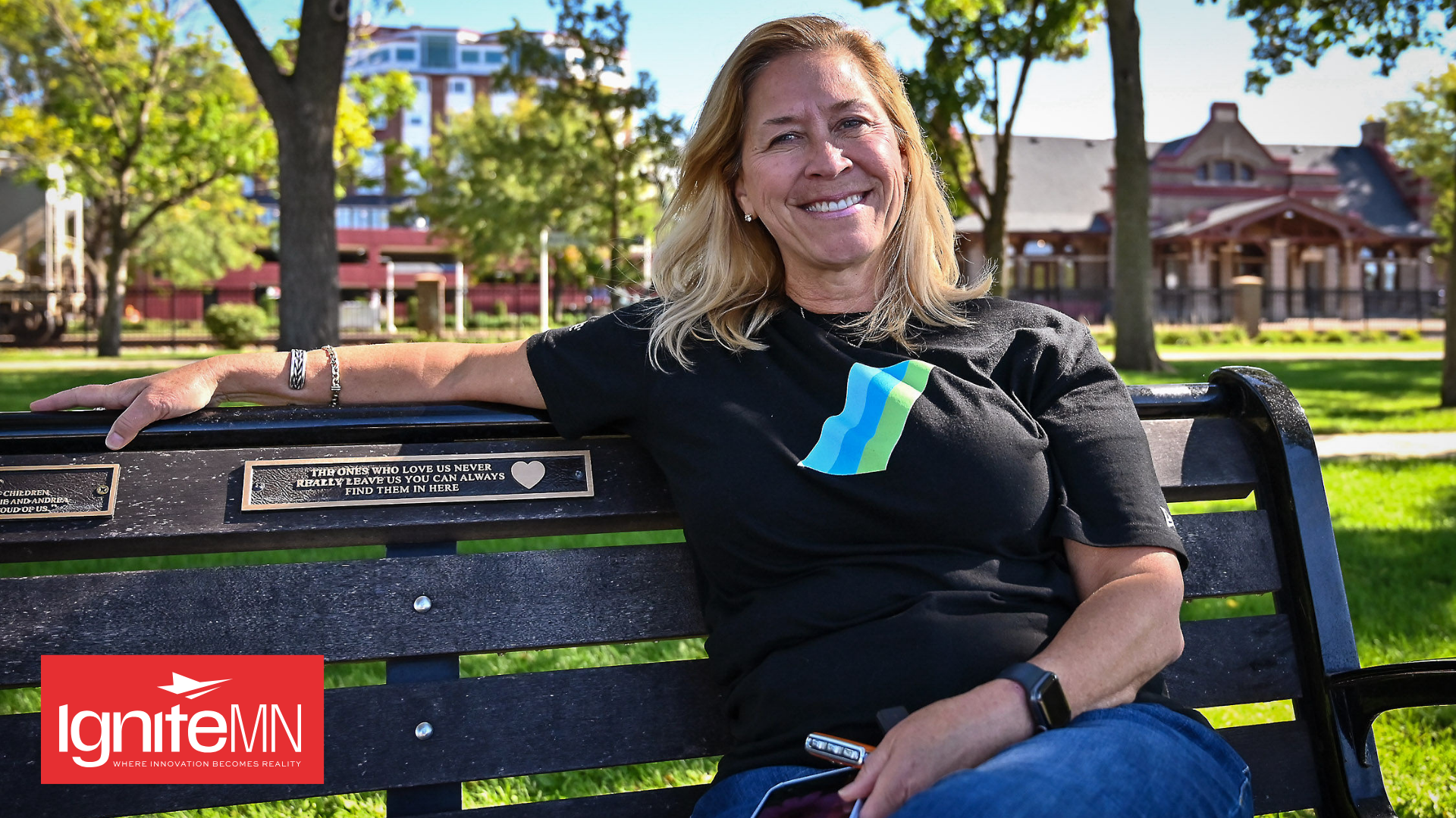 Susan Langer sits on a bench in downtown Red Wing with the IgniteMN logo in the bottom left corner